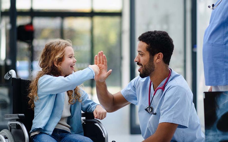 Young multiracial doctor having fun with little girl on wheelchair.