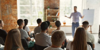 Male speaker giving presentation in hall at university workshop. Audience or conference hall. Rear view of unrecognized participants in audience. Scientific conference event, training. Education