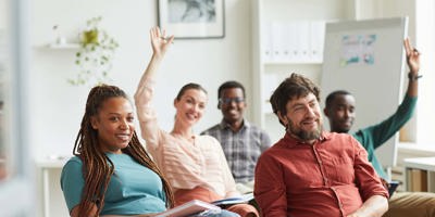 Multi-ethnic group of people raising hands while answering questions during training seminar or business conference in office, copy space