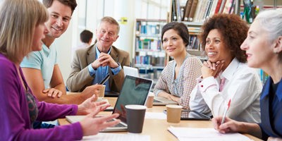 Group Of Mature Students Collaborating On Project In Library