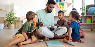 Group of small nursery school children with man teacher sitting on floor indoors in classroom, having lesson.