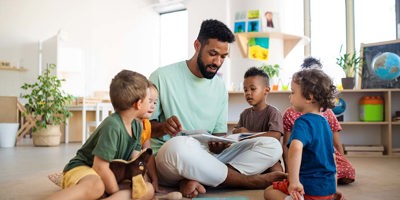 Grupo de pequeños niños de guardería con un maestro sentado en el suelo en el interior del aula, teniendo una lección.